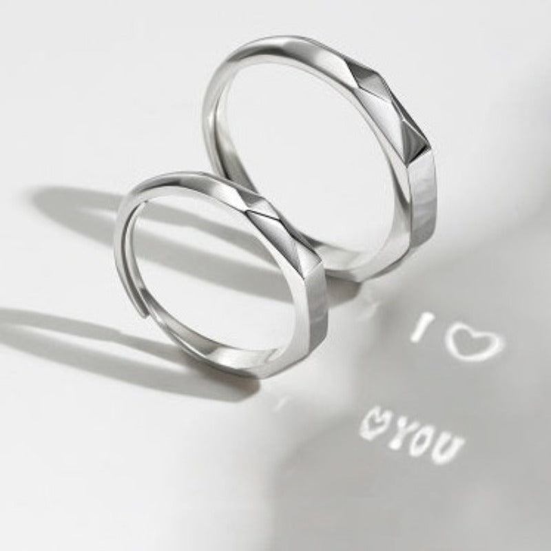 Two S925 Sterling Silver Light Reflection Rings by Jingqian with a faceted design are placed on a white surface. Light reflecting off the rings casts a shadow with the words "I ❤️ YOU" below them.