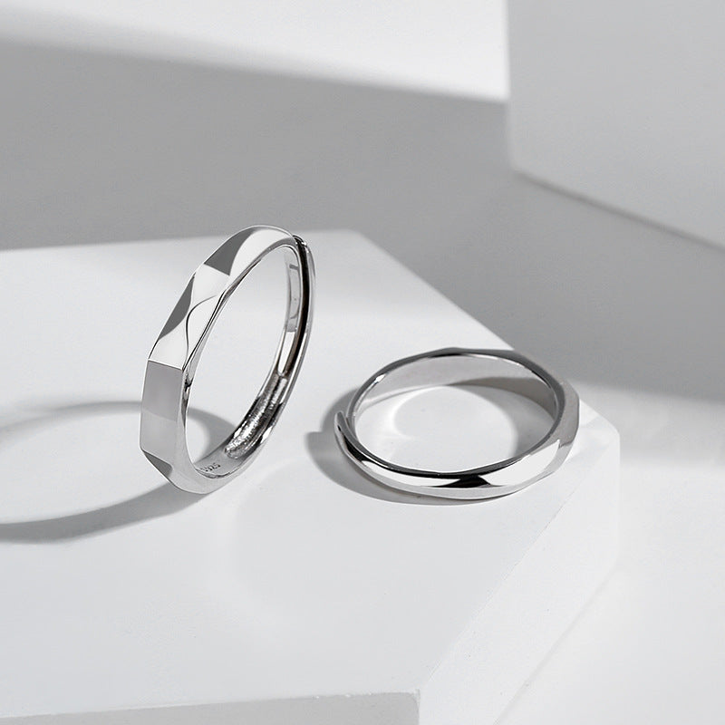Two minimalist, sterling silver rings are displayed on a clean, white surface. The ring on the left has a faceted design, while the one on the right is smooth and plain. Soft lighting casts gentle shadows and highlights light reflections, accentuating the sleek and modern aesthetic of the Jingqian S925 Sterling Silver Light Reflection Ring.