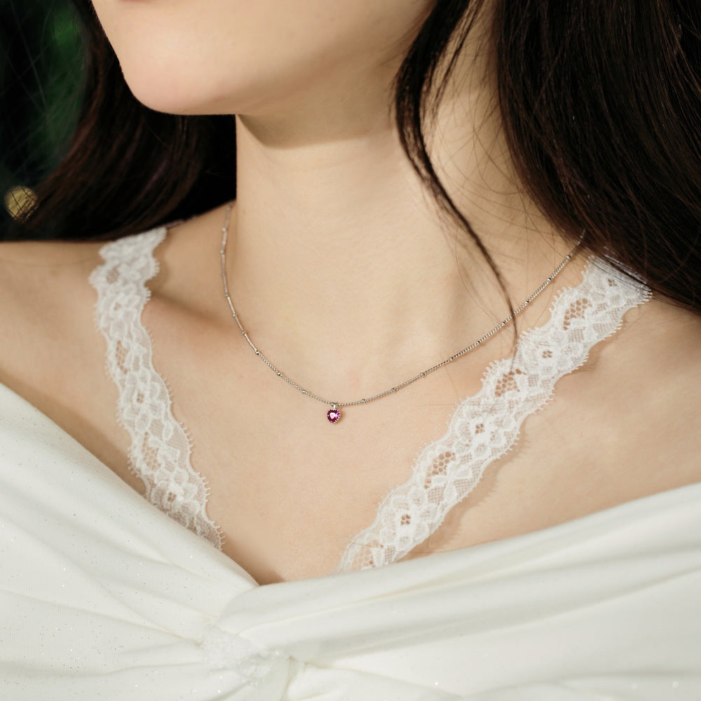 Necklace with a red gemstone worn by a person in a white lace garment.