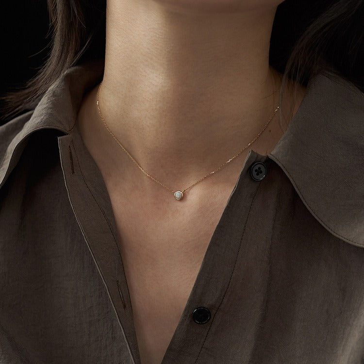 Necklace with a small round pendant worn by a person in a brown shirt.