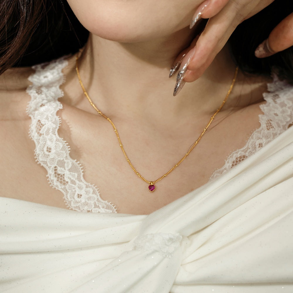 Gold necklace with a red gemstone worn by a person in a white lace garment.