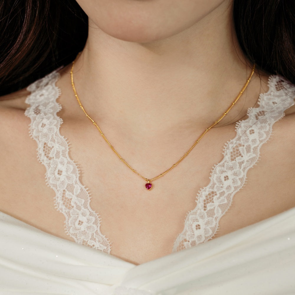 Gold necklace with a red gemstone pendant worn by a person in a white lace garment.