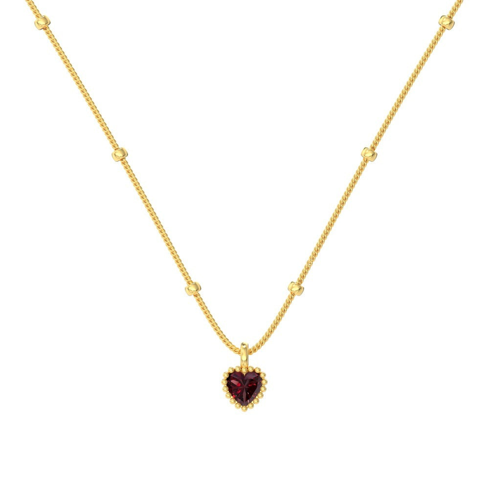 Gold necklace with a heart-shaped red gemstone pendant on a white background